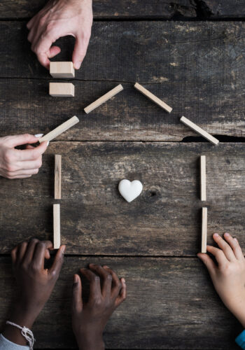 Family of four with kids of caucasian and african american race, building a house of wooden blocks with heart shaped marble inside it.